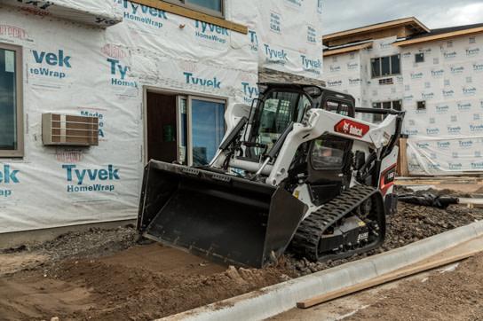 Bobcat T66 spreading base with a bucket beside a new building