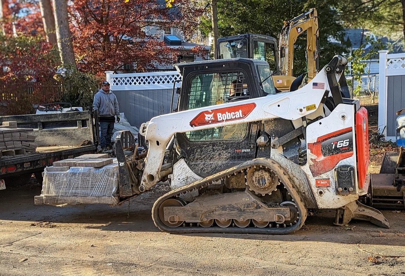 Side view of a Bobcat T66 track loader carrying a pallet of pavers